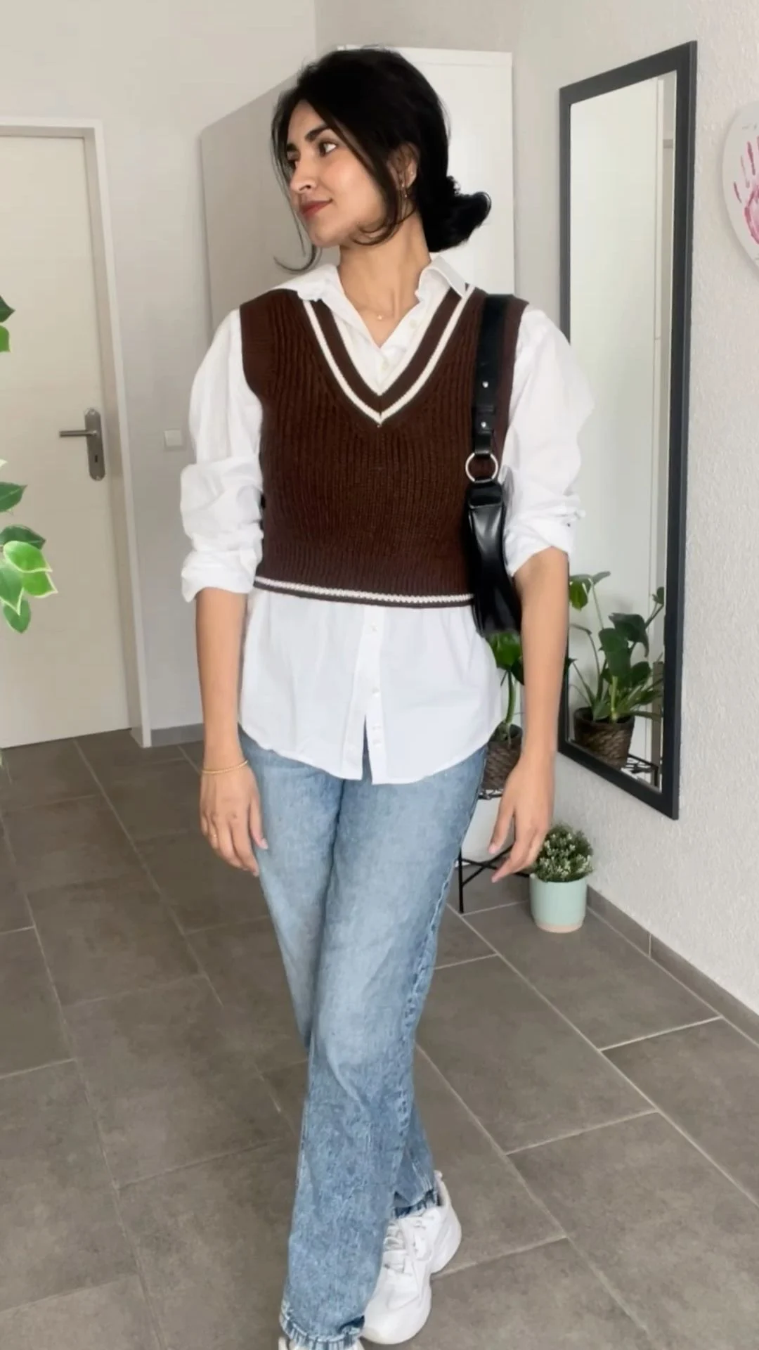 Old money aesthetic outfit with brown striped knit vest over white shirt and light blue jeans